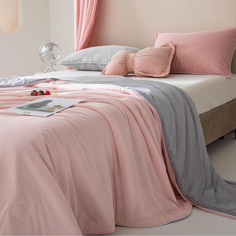 Light pink and gray ice silk quilt neatly spread on a modern styled bed with decorative pillows in bright bedroom.