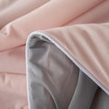 Close-up of soft pink and gray ice silk quilt fabric showing smooth texture and gentle folds.