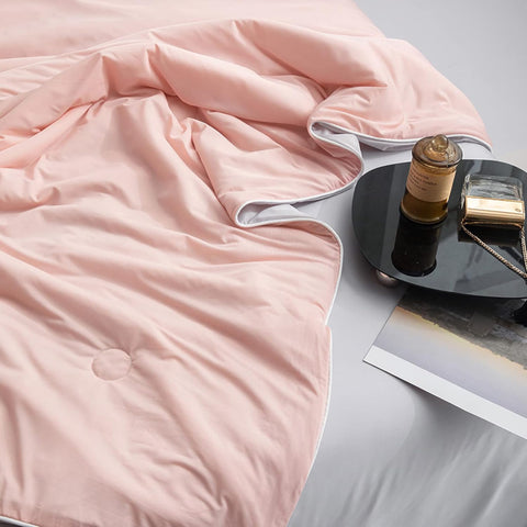 Close-up of soft pink and gray double-layered ice silk quilt draped on black side table
