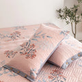 Close-up of pink botanical pillowcases and quilt on bed with summer print
