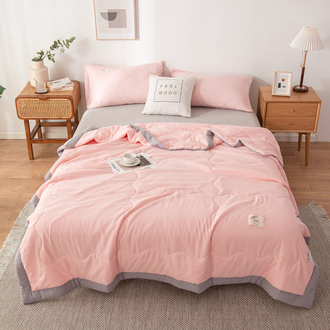 Pink quilt summer on a bed in a bedroom setting with side tables and decor.