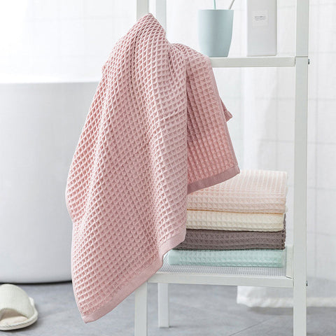Soft pink waffle towel hanging on shelf next to folded towels