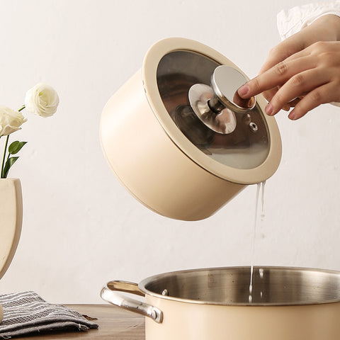 Pouring water from beige saucepan with glass lid in modern kitchen