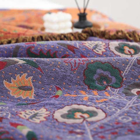 Close-up of purple boho cotton throw blanket showing intricate floral patterns,  and a decorative candle in a wicker tray