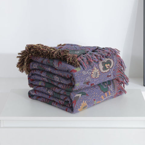 Folded purple boho cotton throw blanket with fringed edges on white surface