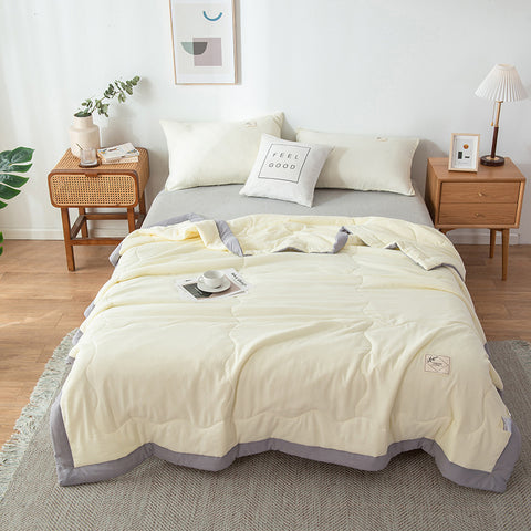 Neatly made bed with a light-colored quilt summer cover ice blanket in a bedroom setting.