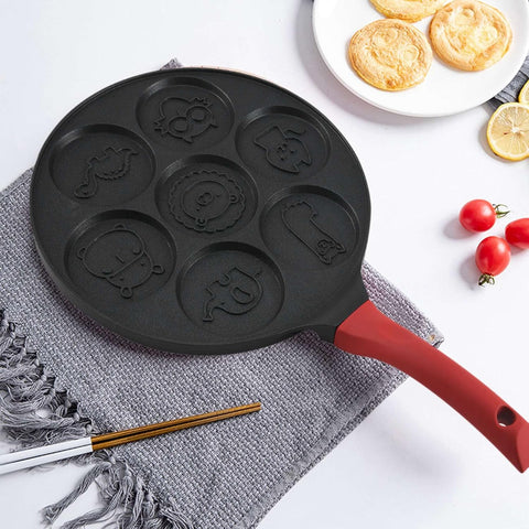 Animals Waffle and Pancake Pan with red handle resting on grey cloth with chopsticks and cooked pancakes on white plate nearby