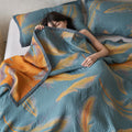 Woman resting under reversible feather cotton quilt in teal and orange