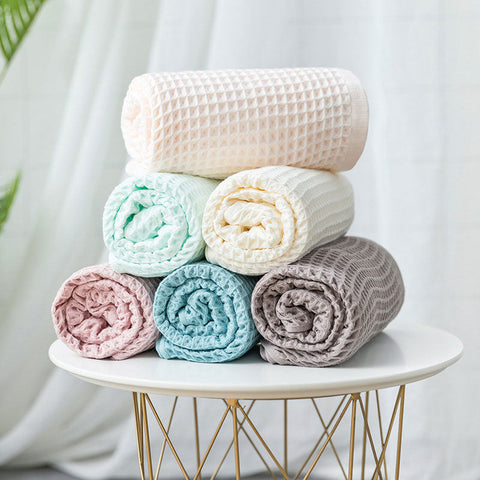 Rolled waffle weave bath towels in beige, mint, gray and pink on gold rack