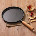 Black frying pan with wooden handle on a wooden surface
