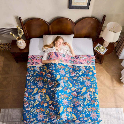 Top view of woman lying in bed under a Royal flora cotton blanket in a bedroom setting.