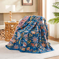 Floral patterned blanket draped over a chair in a room with a lamp and wooden side table.
