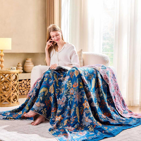 Woman sitting on a couch with a floral cotton blanket draped over her, in a cozy living room while reading a magazine.