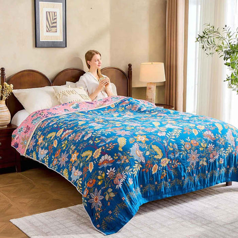 Woman sitting on a bed with a colorful floral quilt in a bedroom setting while looking at window thinking. 