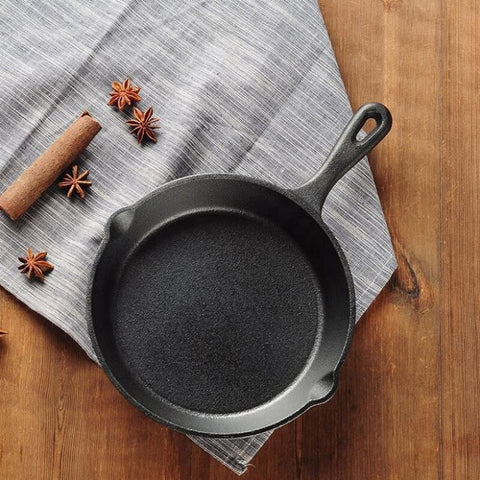 Black cast iron skillet on a wooden surface with cinnamon sticks and star anise.