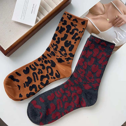 A pair of retro leopard print socks displayed on a table, with one sock in black and the other in a brown color, both featuring a leopard print pattern.