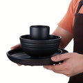Person holding a set of black wheat straw dishes including a bowl, mug, and plate.