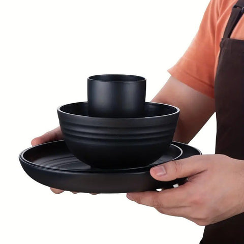Person holding a set of black wheat straw dishes including a bowl, mug, and plate.