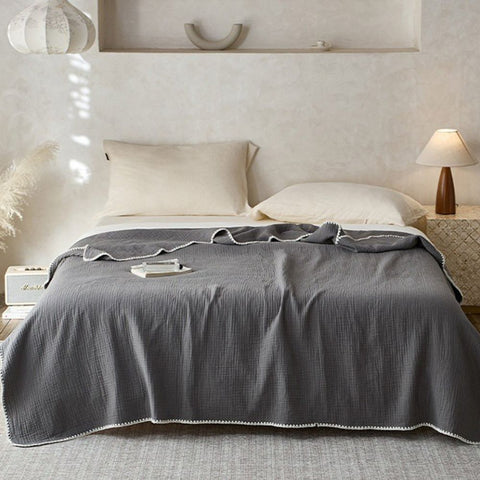Slate gray muslin cotton blanket with white trim on minimal bedroom setup