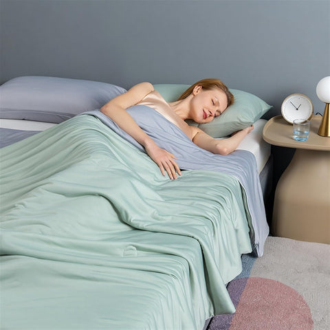 Woman peacefully sleeping under a mint green and light grey ice silk quilt in a modern bedroom setting with soft lighting