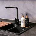 Black kitchen faucet over a sink with two soap dispensers labeled 'HANDS' and 'DISHES' on a gray countertop.