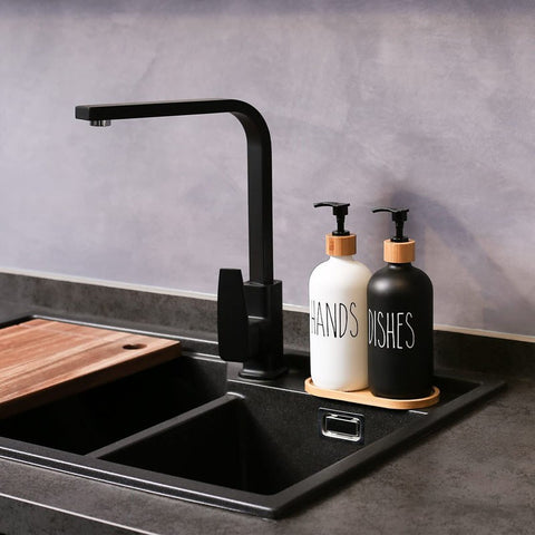 Black kitchen faucet over a sink with two soap dispensers labeled 'HANDS' and 'DISHES' on a gray countertop.