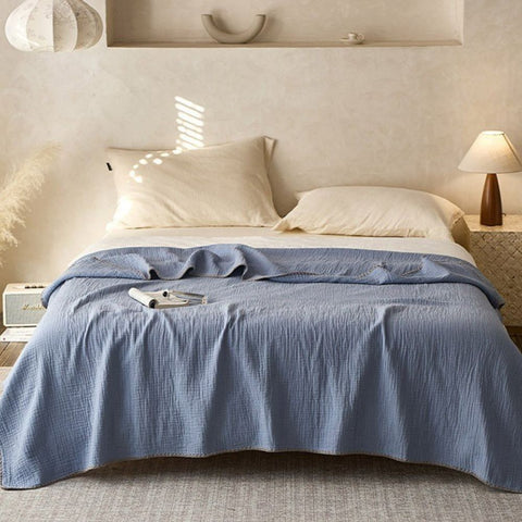 Soft blue muslin blanket with textured cotton layers draped on modern bed