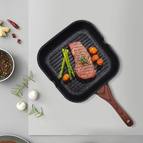 Grilled steak with vegetables on a black grill pan with a wooden handle, on a light gray background.