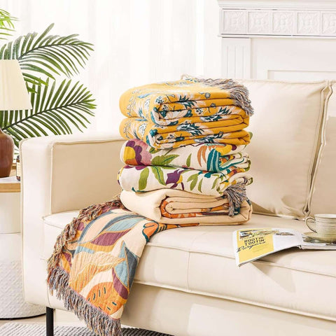 Stack of colorful patterned blankets on a beige sofa with a plant in the background
