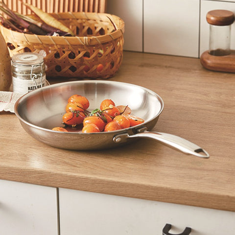 Stainless steel frying pan with tomatoes on a wooden kitchen counter