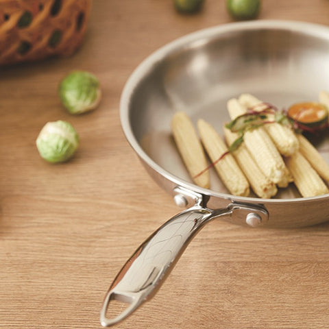 Stainless steel frying pan with food on a wooden surface