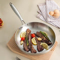 Stainless steel frying pan with cooked meat and vegetables on a beige surface