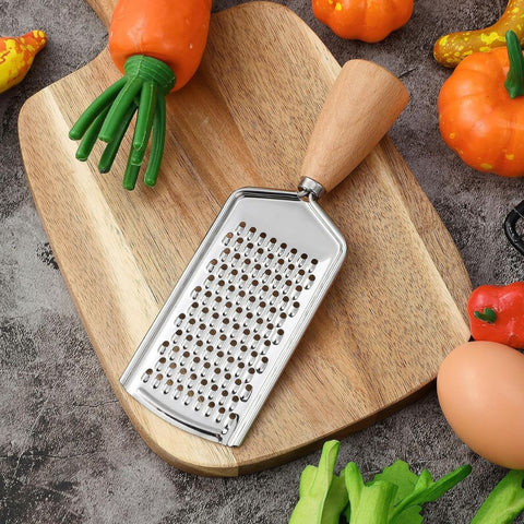 Stainless steel handheld grater with wooden handle on cutting board with fresh vegetables