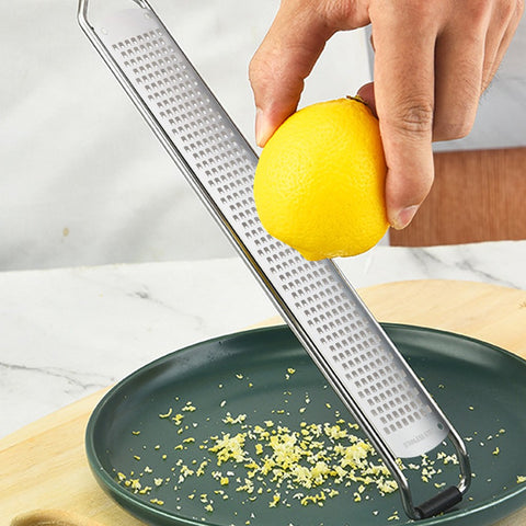 Hand zesting lemon over a green plate using stainless steel grater with wooden handle