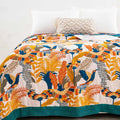Bright cotton throw blanket with colorful songbird and botanical design spread across a cozy bed with white pillows
