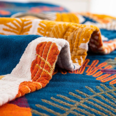 Close-up of textured cotton throw blanket with warm terracotta, blue, and cream botanical pattern and stitched edge detail