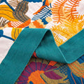 Close-up detail of colorful cotton throw blanket with bird and botanical patterns and teal fabric border
