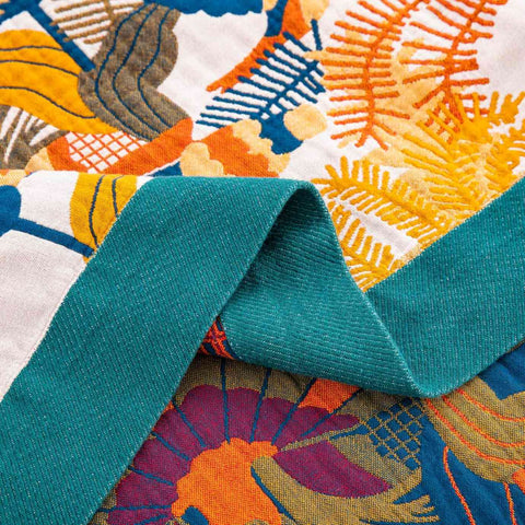 Close-up detail of colorful cotton throw blanket with bird and botanical patterns and teal fabric border