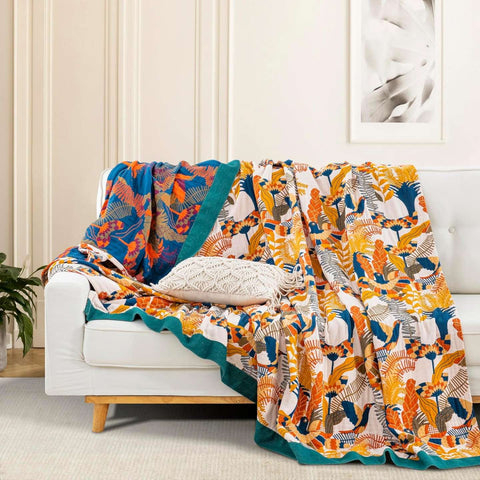 Colorful cotton throw blanket with bird and botanical patterns draped over a white sofa with decorative pillow in a bright living room