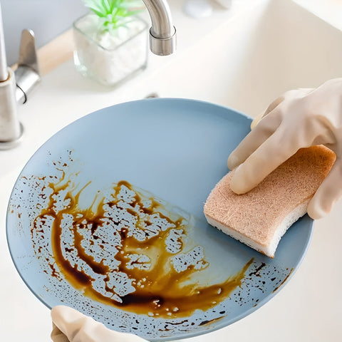Person cleaning a greasy plate with a sponge in a kitchen setting