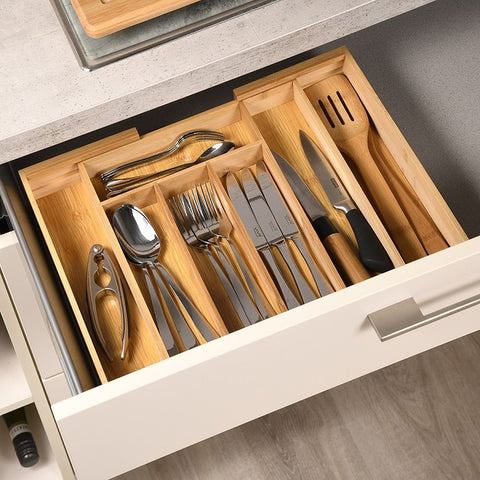 Wooden cutlery organizer with silverware in a kitchen drawer.