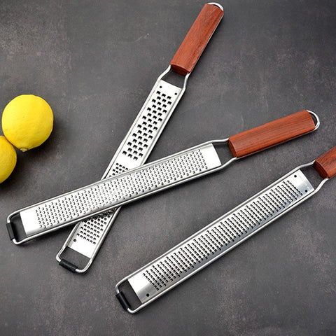 Three wooden handle stainless steel graters with lemons on dark surface