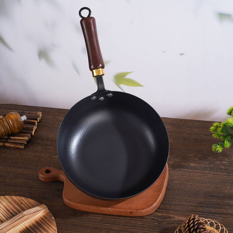  Top view of hammered iron wok with wooden handle on wooden board and table