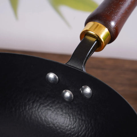 Top view of hammered iron wok with wooden handle on wooden board and table