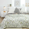 Cotton quilt with bird and tree print in light green tones styled on a modern white bed