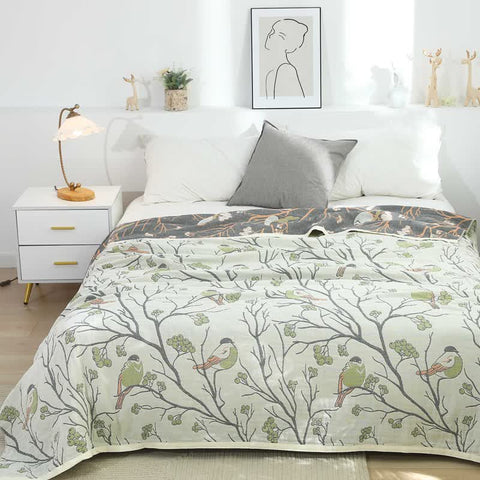 Cotton quilt with bird and tree print in light green tones styled on a modern white bed