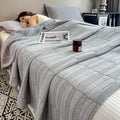 Gray cotton muslin quilt on bed with candle and magazine