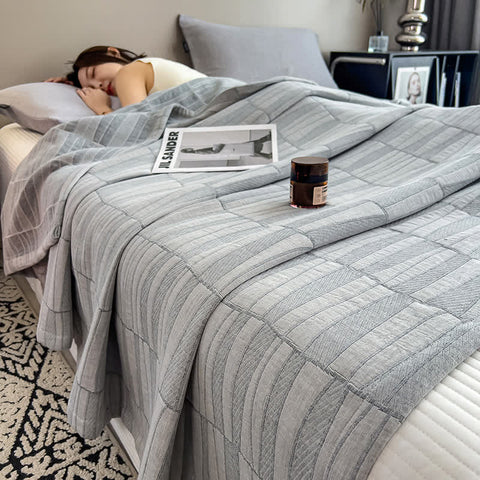 Gray cotton muslin quilt on bed with candle and magazine