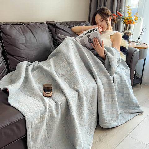 Woman reading with light blue cotton quilt draped over legs on sofa