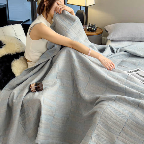 Woman sitting in bed wrapped in light blue cotton muslin quilt